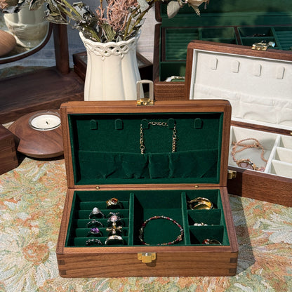 Wooden jewelry box with green interior displaying various jewelry items on a floral background.